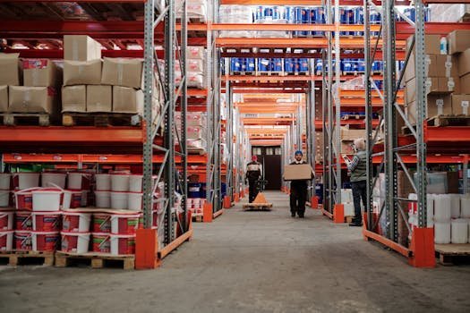 Warehouse interior showing workers handling boxes and organized shelves filled with products.